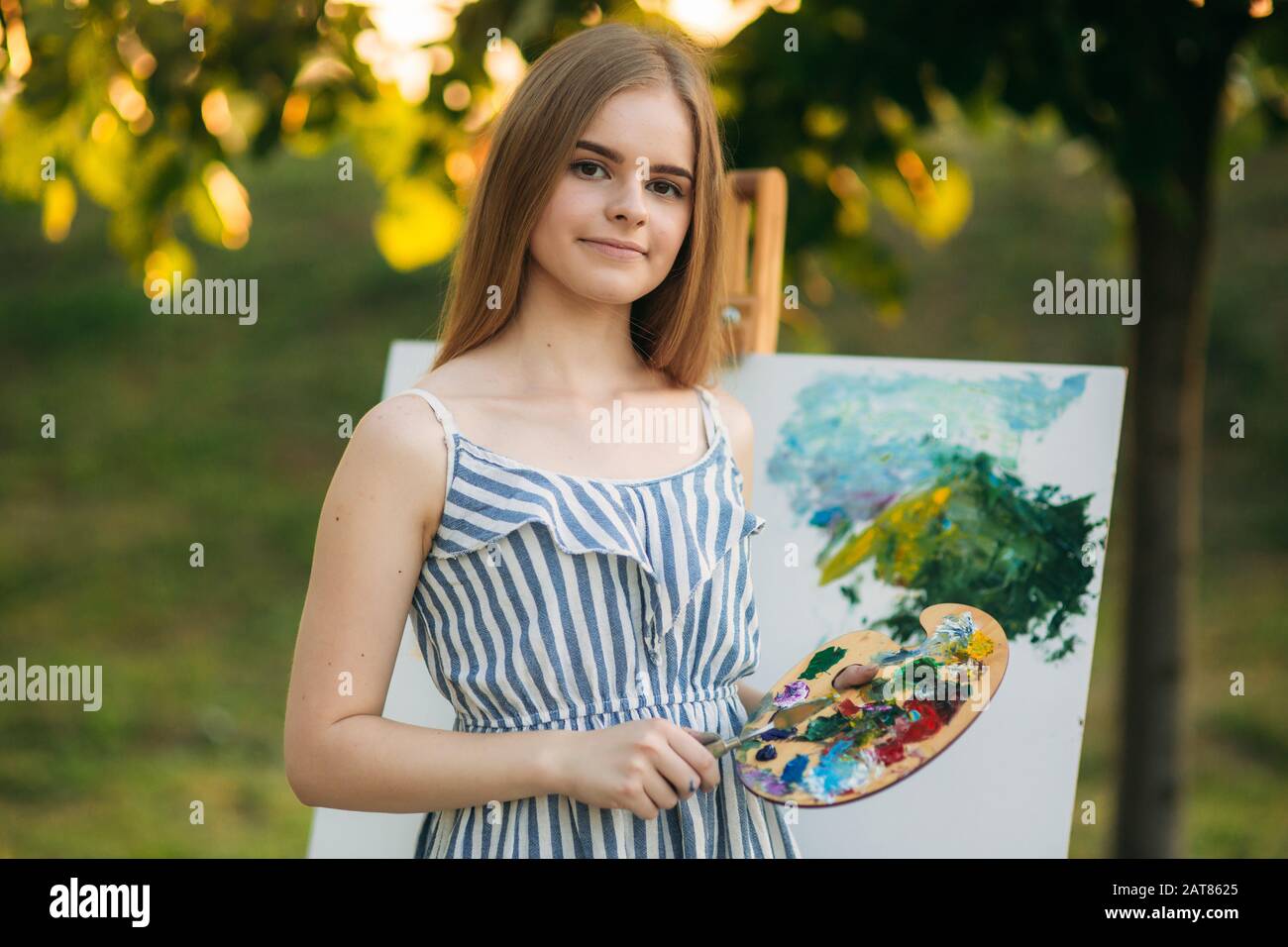 Beautiful girl draws a picture in the park using a palette with paints ...