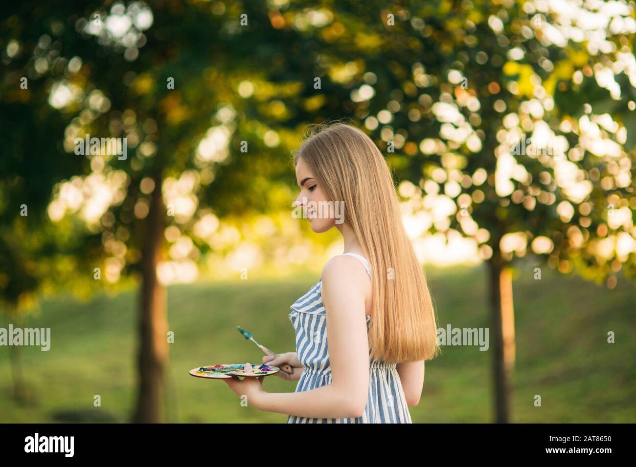 Beautiful girl artist is standing in the park and holding palette with ...