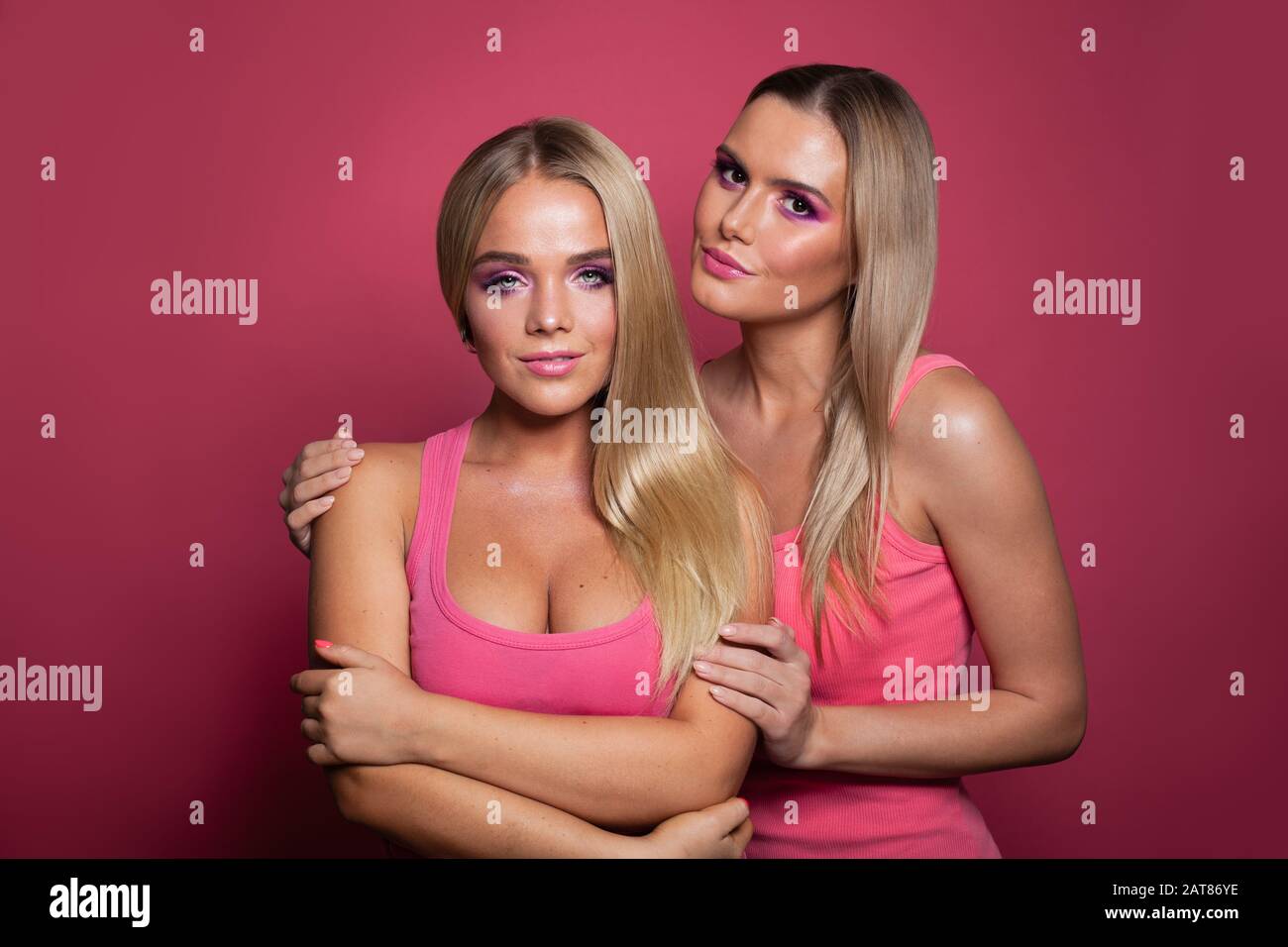 Two blonde models girls in pink shirt on pink background Stock Photo