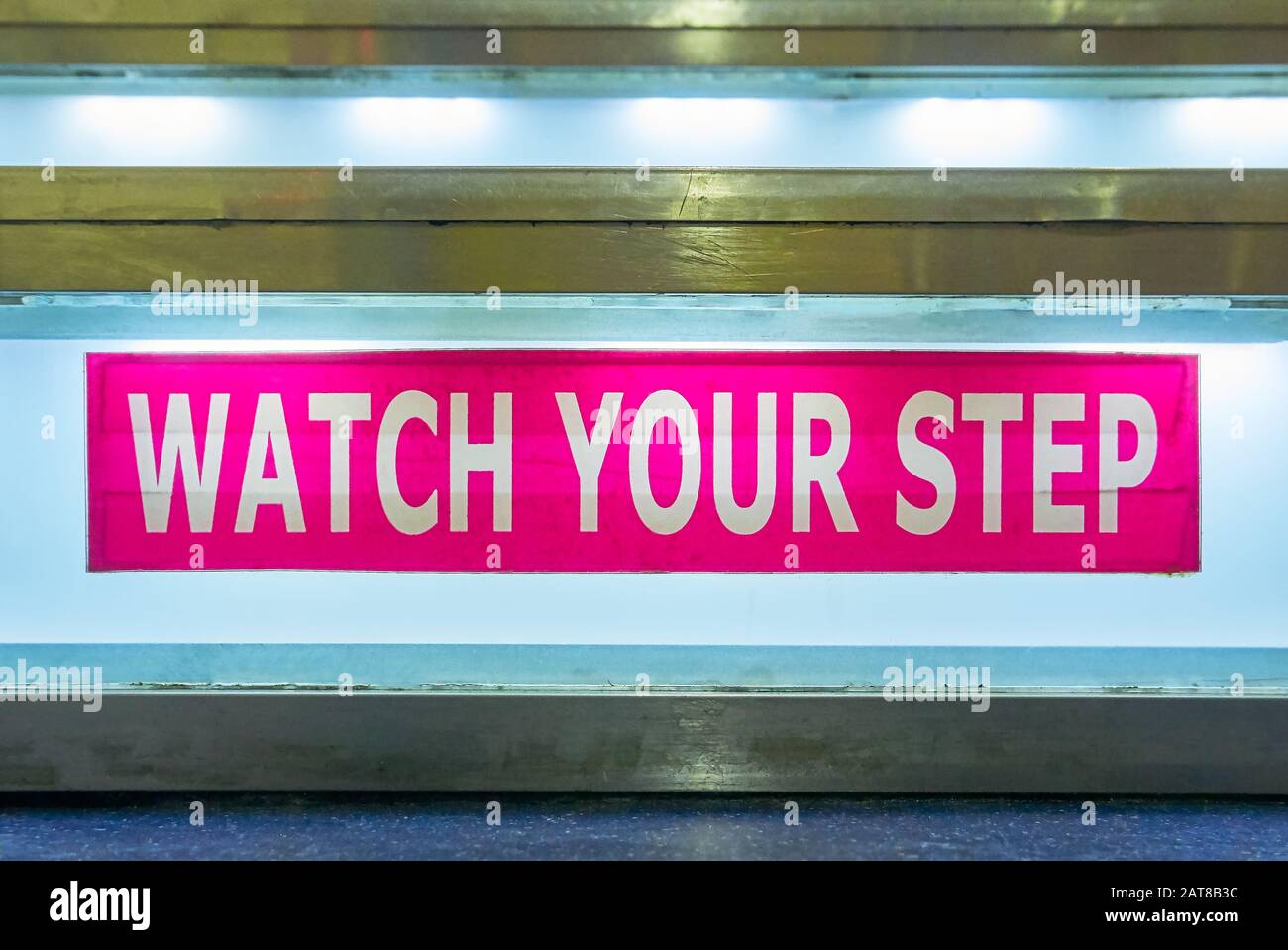 Close-up of a pink colored Watch Your Step sign taped to a staircase, which is illuminated with neon light, seen on a ferry ship in the Philippines Stock Photo