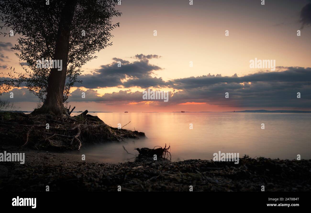 Romantic and quiet sun set by the lake with tree and beach in foreground, beautiful color composition Stock Photo