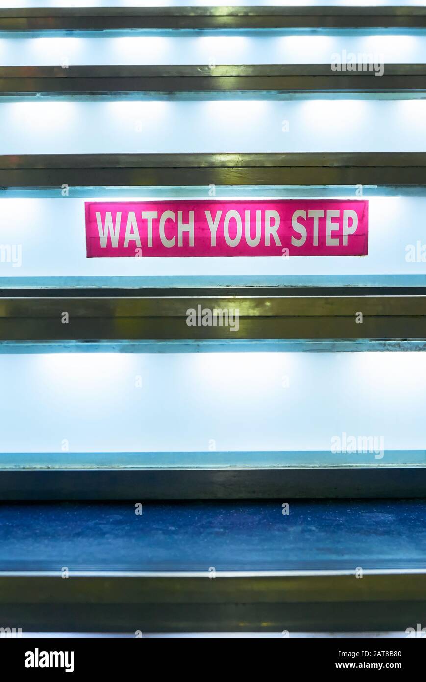 Close-up of a pink colored Watch Your Step sign taped to a staircase, which is illuminated with neon light, seen on a ferry ship in the Philippines Stock Photo