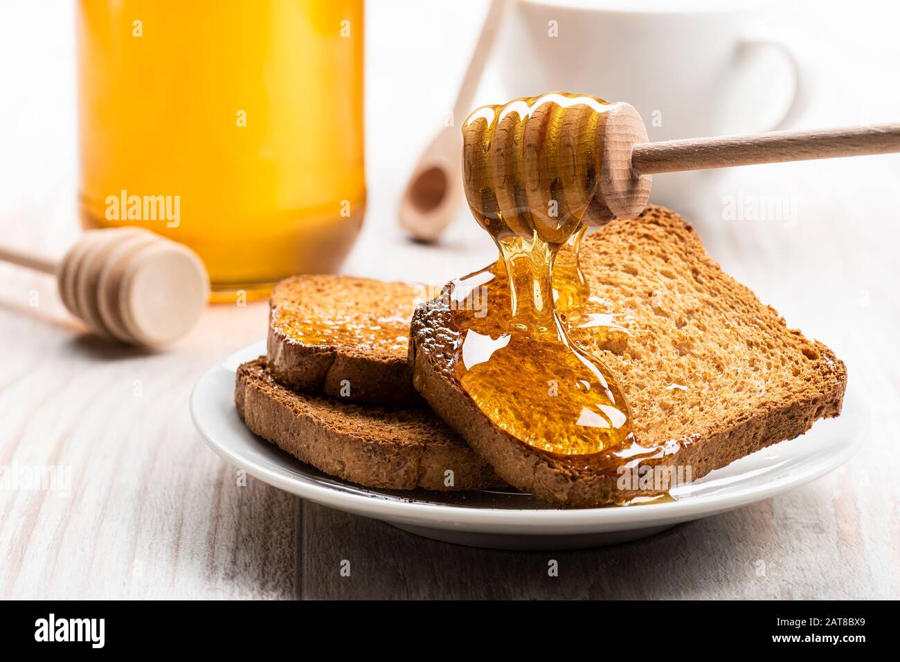 Honey dripping from wooden dipper on some wholemeal rusks. Stock Photo