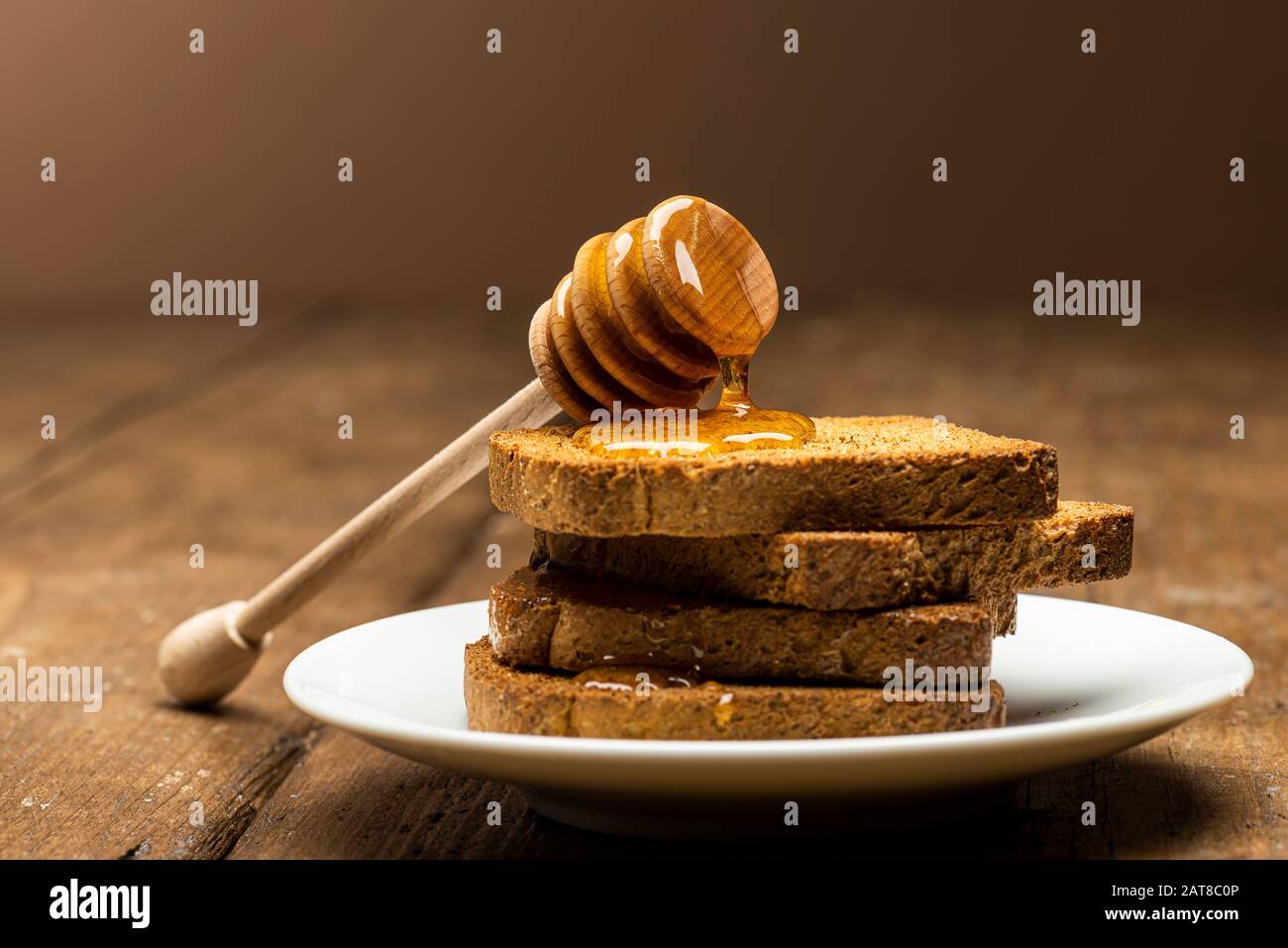 Honey dipper resting on some wholemeal rusks on table. Stock Photo
