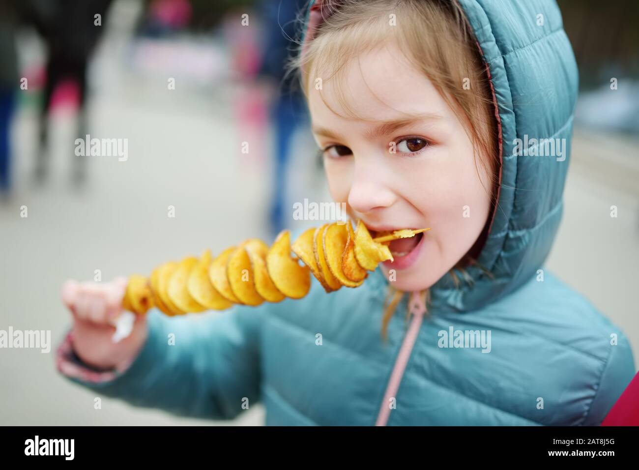 Cute little girl eating fried potato on a stick on cold winter day