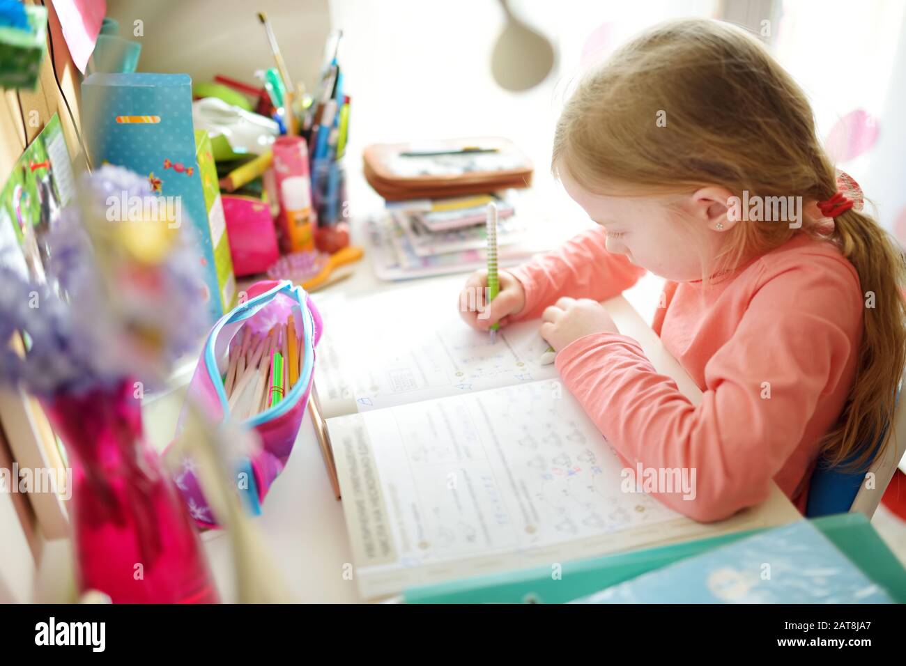 Smart Little Schoolgirl Doing Her Homework At Her Table At Home