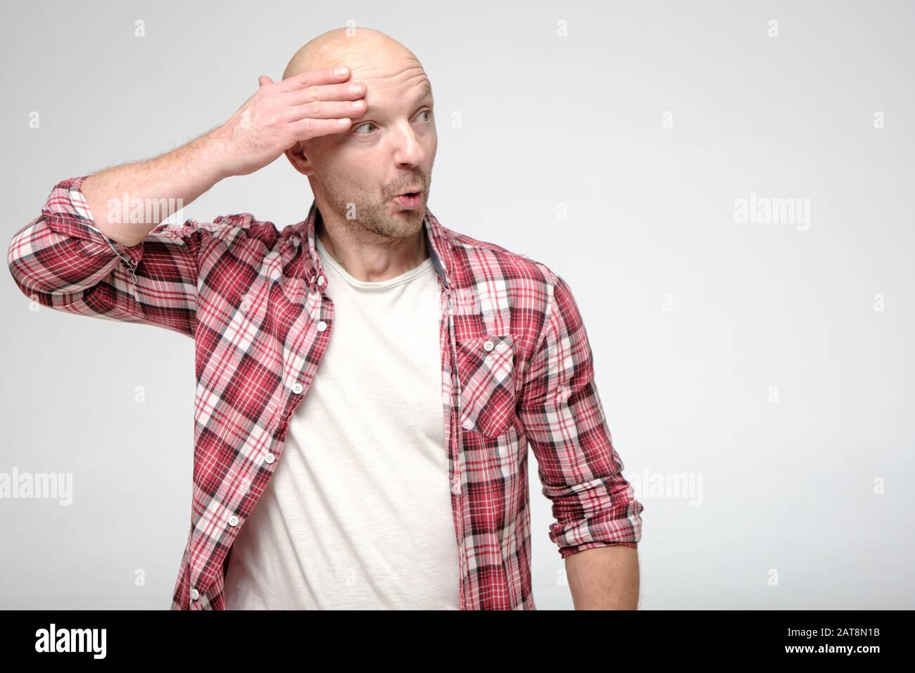 Funny, shocked bald man, with a bizarre expression on face, holds hand near head and looks surprised to the side. Copy space. Stock Photo