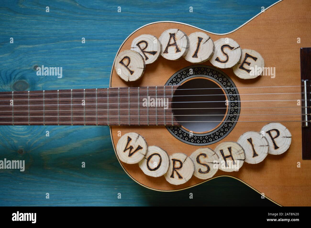 guitar on teal wooden background with wood pieces on it lettering the words: PRAISE and WORSHIP Stock Photo