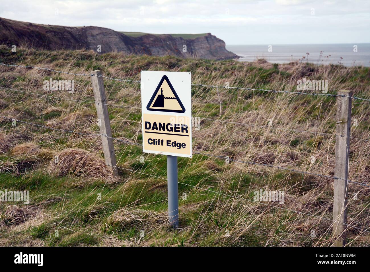 A danger sign warning of a cliff edge, along the Cleveland Way, a hiking trail in North York Moors National Park, Yorkshire, England, United Kingdom. Stock Photo