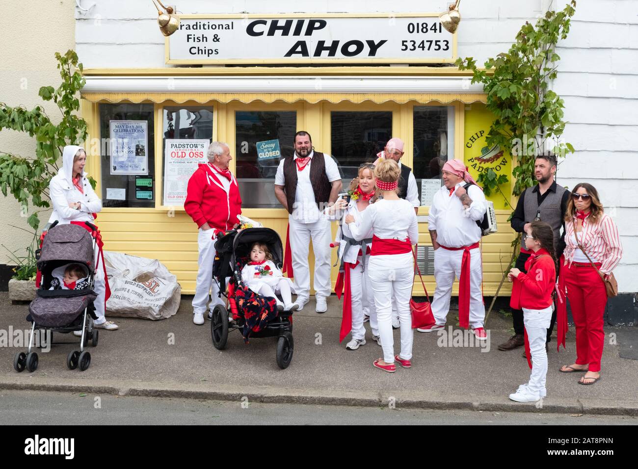 Family wearing red ribbons outside the Chip Ahoy fish and chips shop during the Obby Oss celebrations, Padstow, Cornwall, UK Stock Photo
