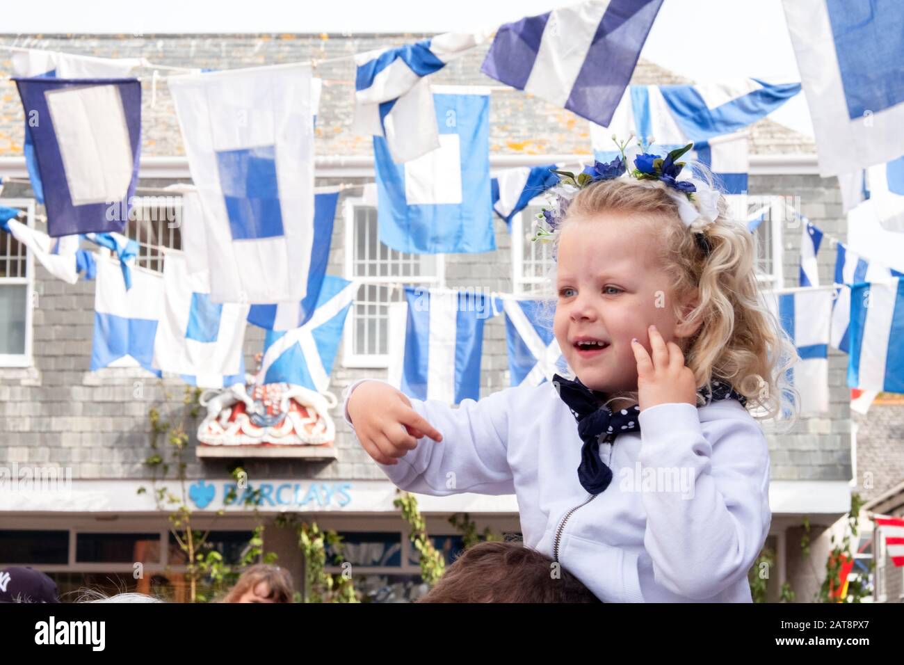 Young girl wearing blue flowers in her hair and smiling with traditional blue and white flags, Obby Oss procession, Padstow, Cornwall, UK Stock Photo