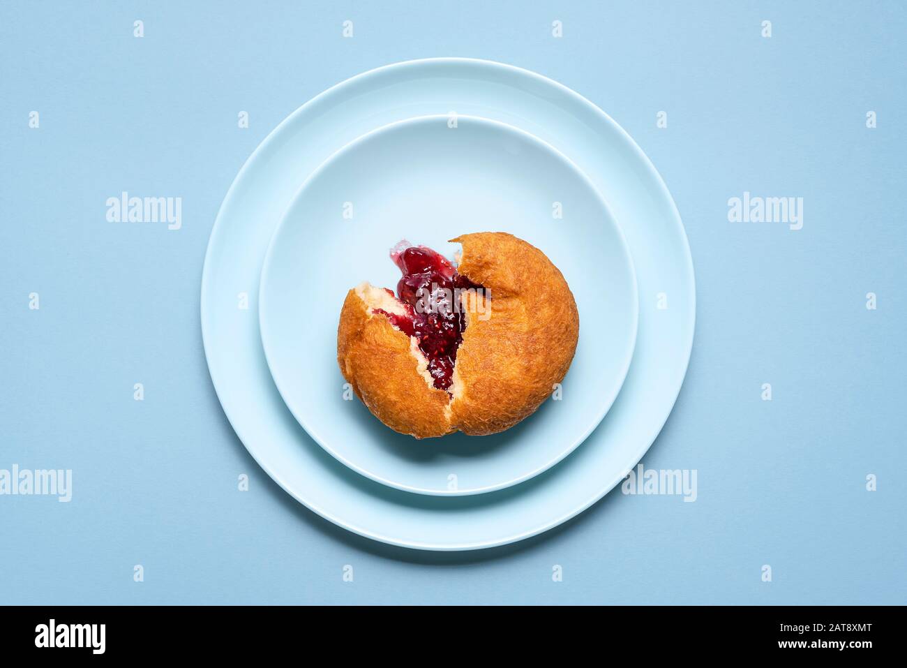 Single berliner doughnut sliced, with raspberry jam on blue plates and seamless background