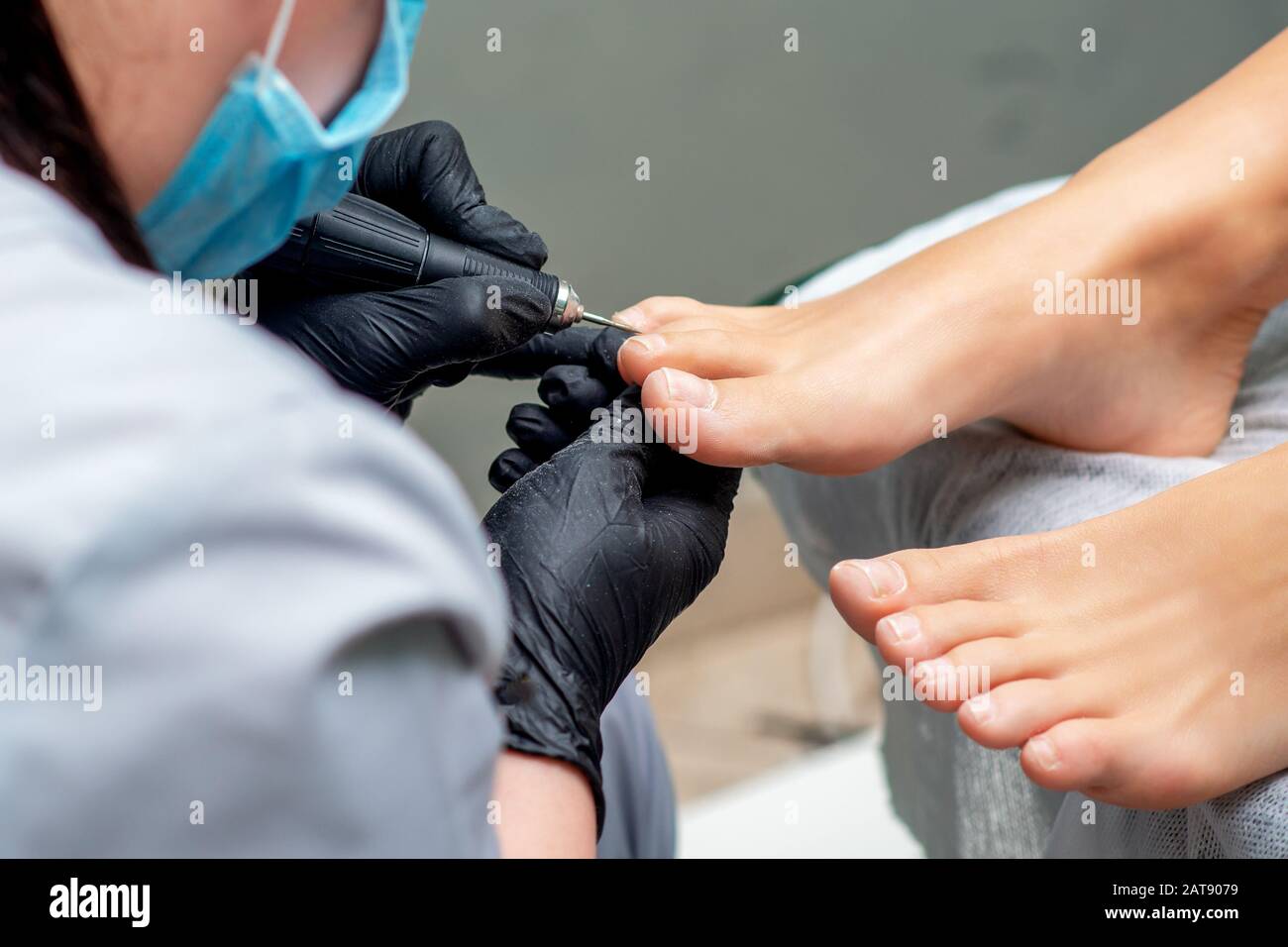 Pedicurist's hands in gloves with special tool doing pedicure of female