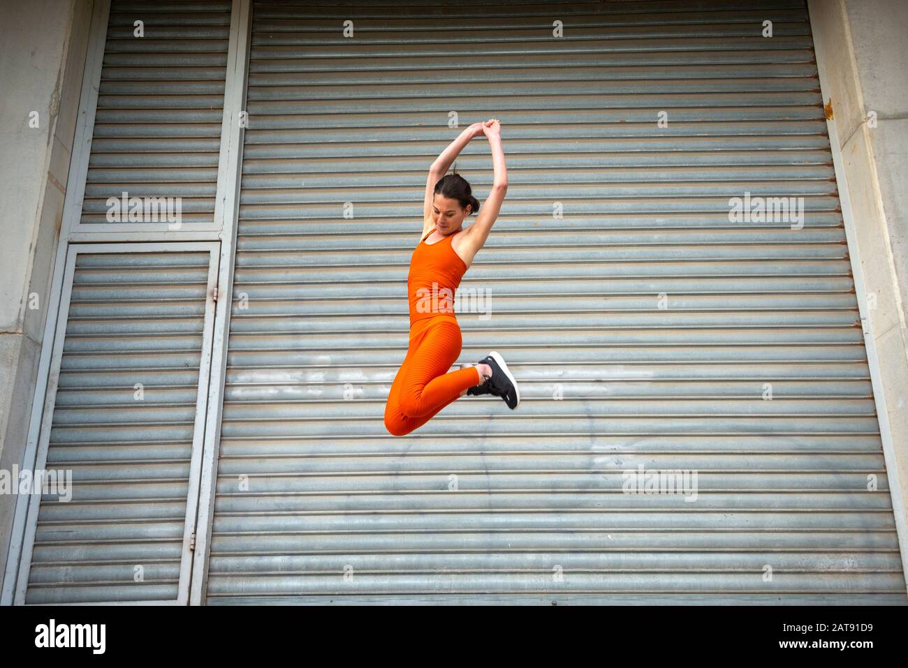 fit woman wearing orange sportswear jumping, urban background. Stock Photo