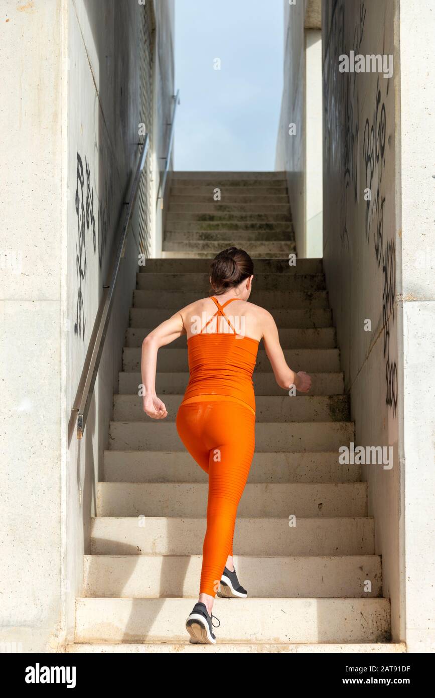 sporty woman running up concrete steps, wearing orange sportswear. fitness training concept. Stock Photo
