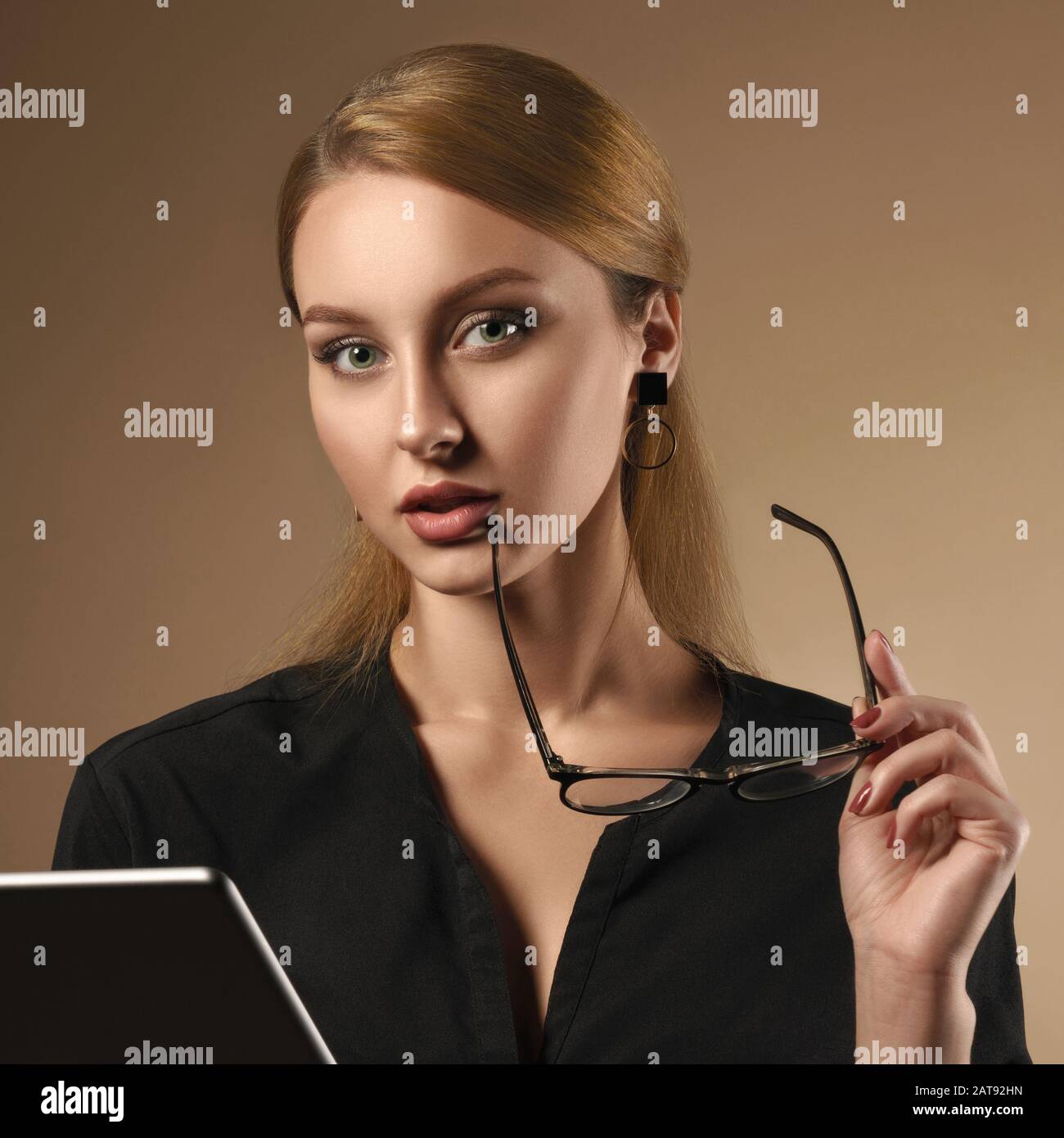 Girl wearing black shirt holding eye glasses while using tablet on beige background Stock Photo