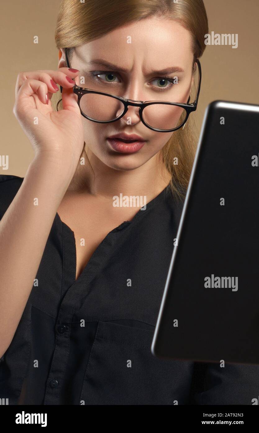 Confused girl taking off eye glasses and looking at the tablet Stock Photo