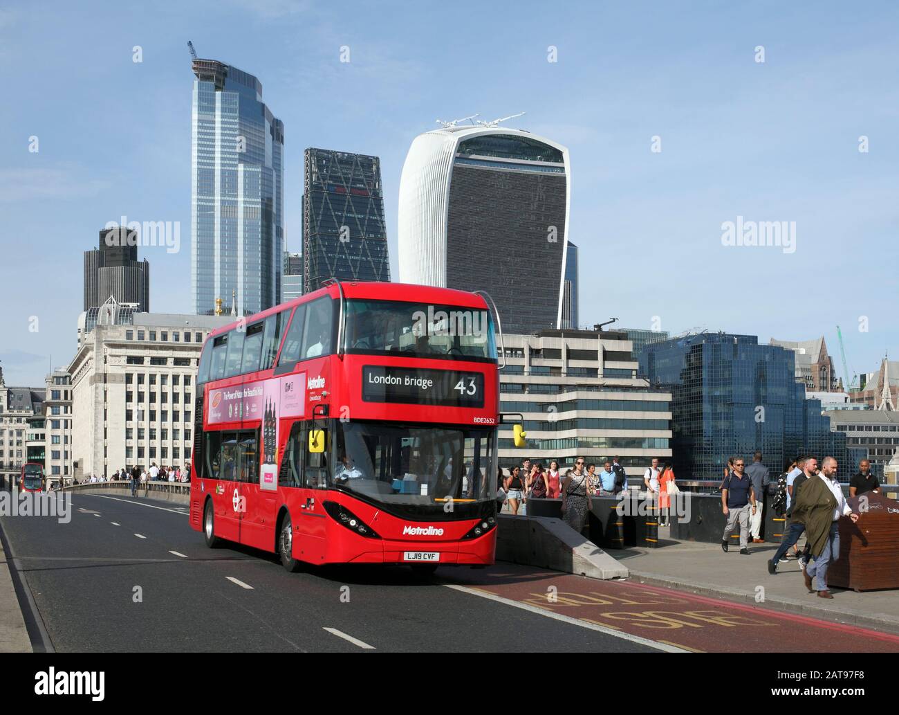 An electric (battery powered) double decker bus crossing London Bridge, London. Background: high rise buildings in the City of London. Stock Photo