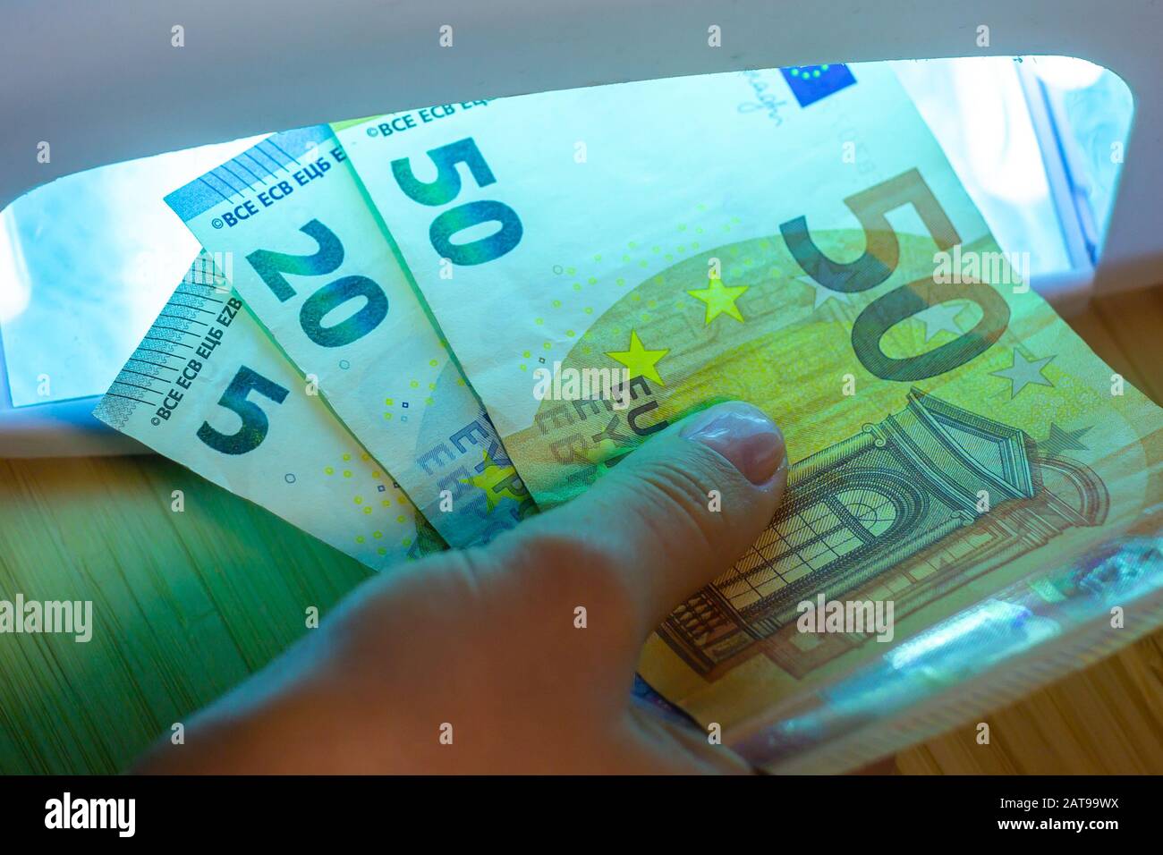 Expert checks paper euro banknotes with infrared or ultraviolet light detector. Stock Photo