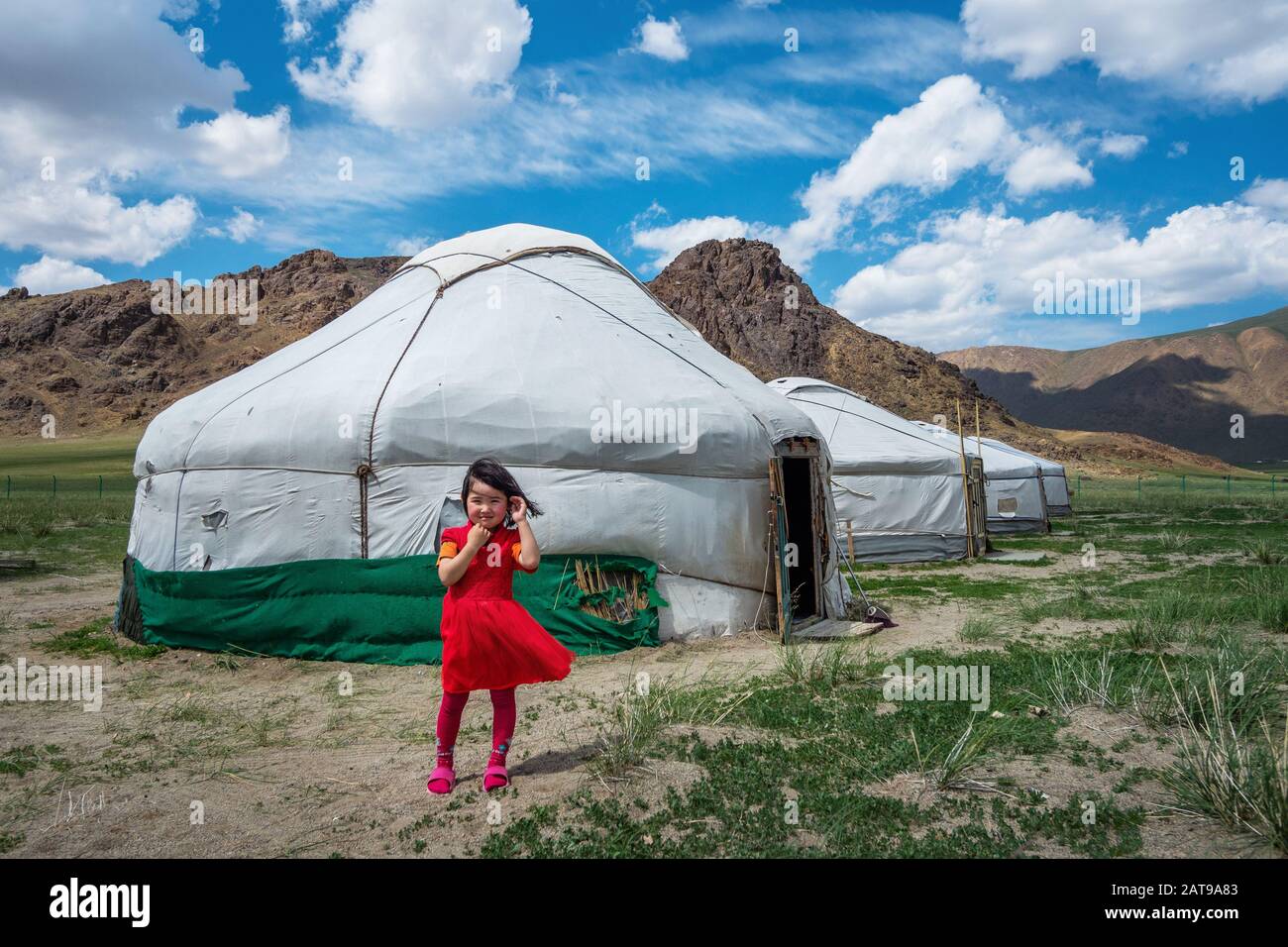Mongolian girl in front of traditional yurts (Mongolian gers) on a sunny day in Bayan-Olgii, West Mongolia. Stock Photo