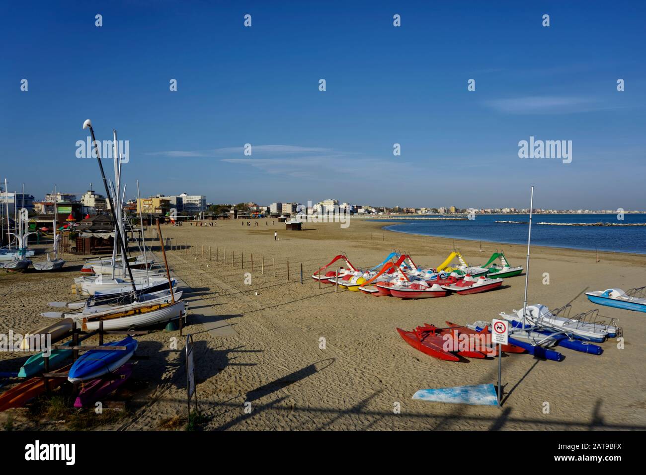 Rimini, Italy - October 21, 2019: View of seafront with yachts, boats, pedalos and canoes on the beach and buildings in the background. Stock Photo