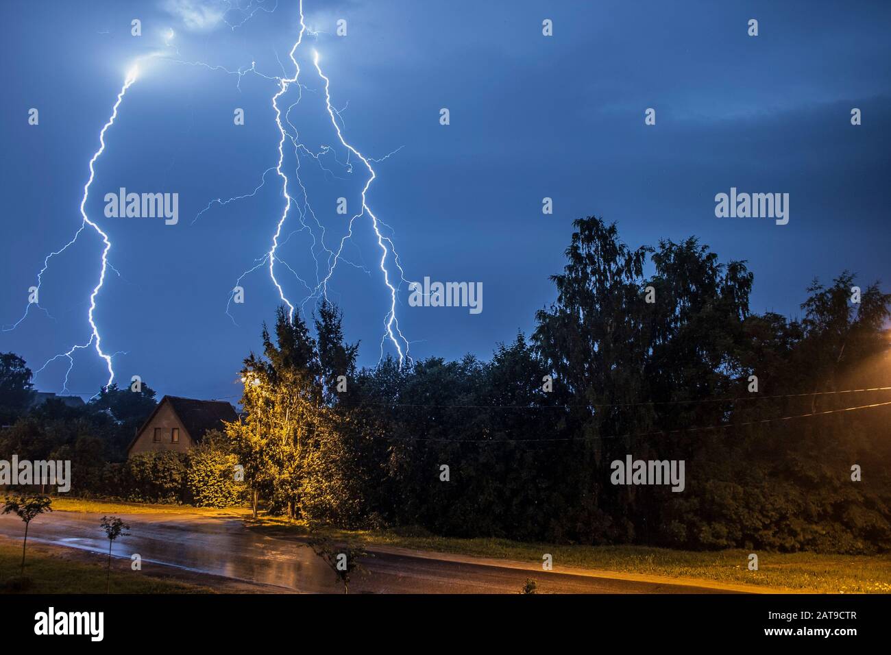 Thunder lightning on a summer night over a small village with trees and houses Stock Photo