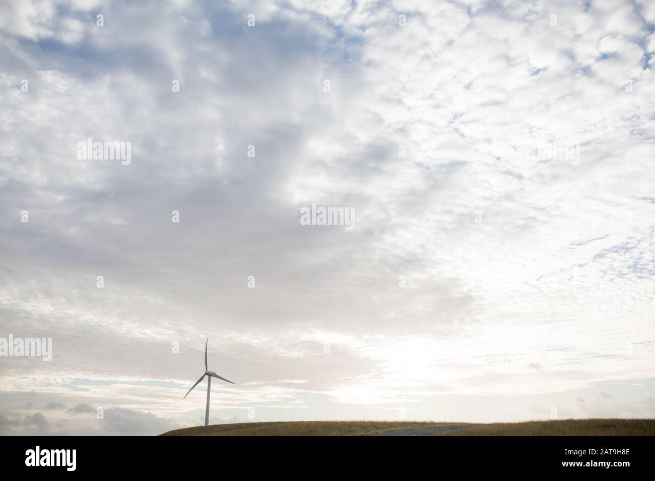 a wind turbine used in energy production on a hill with setting sun behind Stock Photo