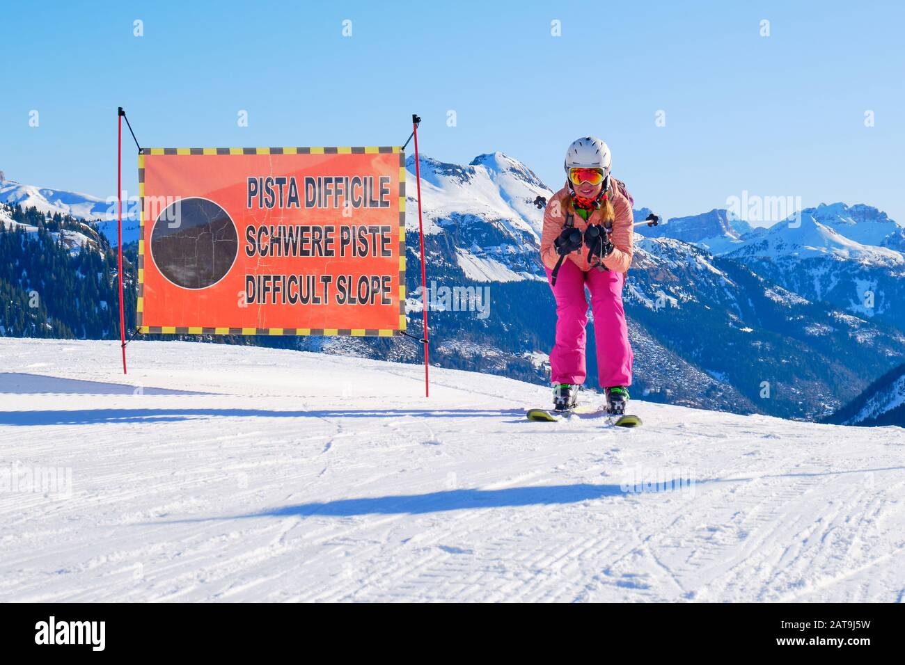 Skier posing in a race style position next to a ski piste sign saying Difficult Slope in German, Italian, and English, in Dolomiti Superski domain, It Stock Photo