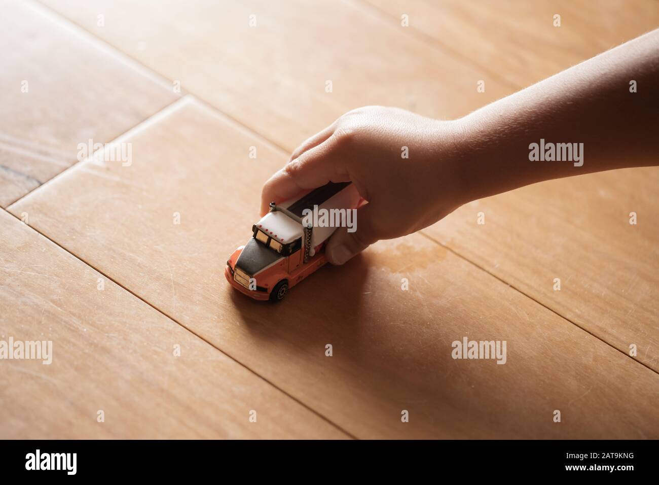 A preschool age child's hand playing with toy truck on wooden floor, imaginative play Stock Photo