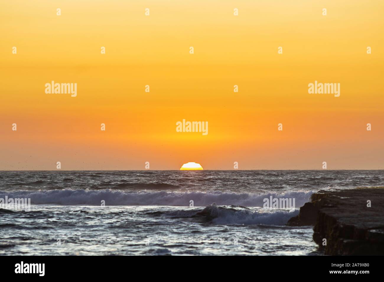 An amazing view of the sunset over the water in the Chilean coast. An idyllic beach scenery with the sunlight illuminating the rocks Stock Photo