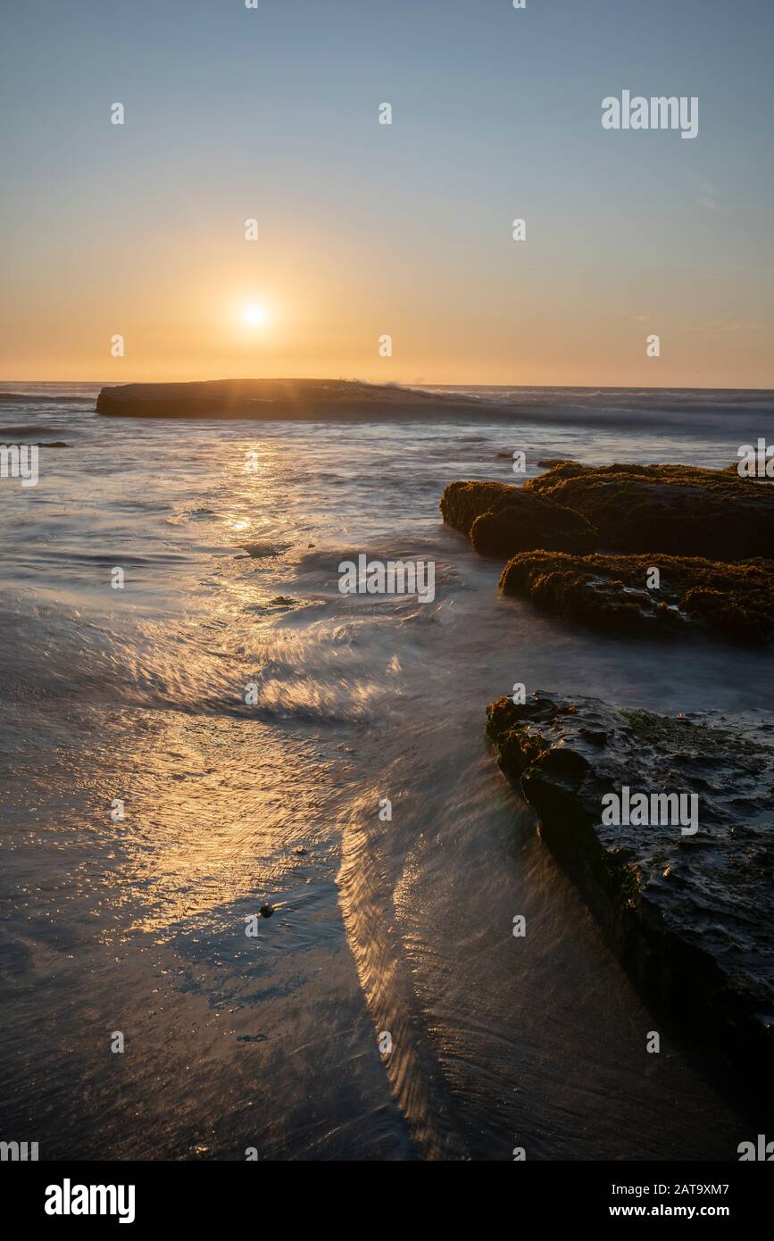 An amazing view of the sunset over the water in the Chilean coast. An idyllic beach scenery with the sunlight illuminating the green algae and rocks Stock Photo