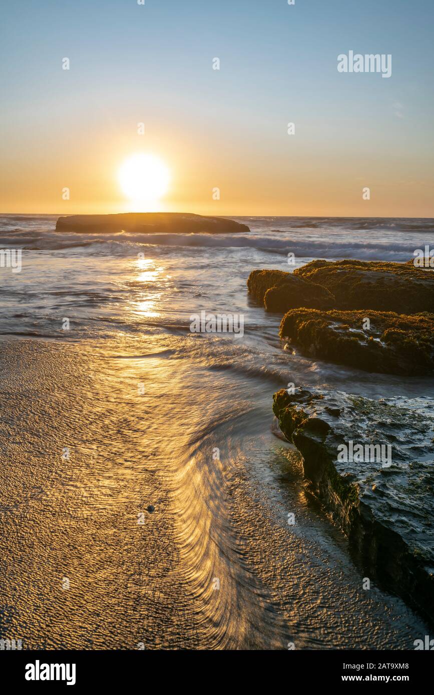 An amazing view of the sunset over the water in the Chilean coast. An idyllic beach scenery with the sunlight illuminating the green algae and rocks Stock Photo