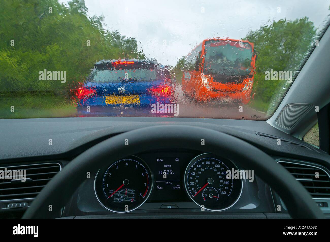 Dashboard and wet car glass with another blurred car and bus in the background Stock Photo