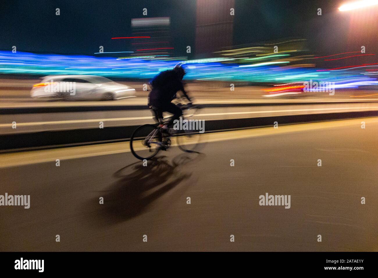 A cyclist leaves work and cycles fast at night to go home Stock Photo