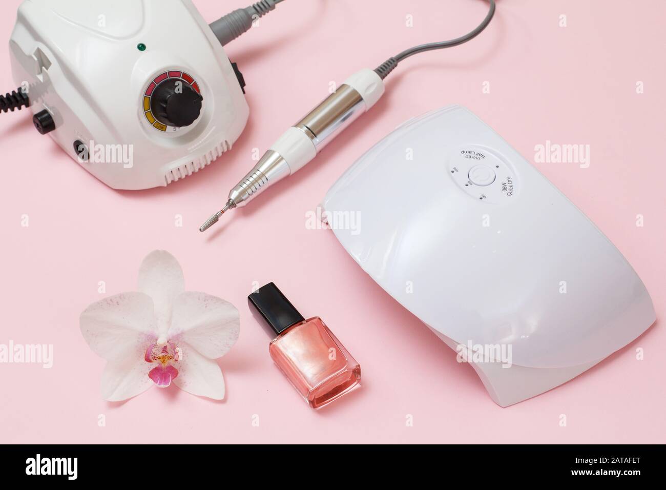 Milling cutter, led UV lamp, nail polishes and orchid flower on a pink background. A set of cosmetic tools for professional hardware manicure. Top vie Stock Photo