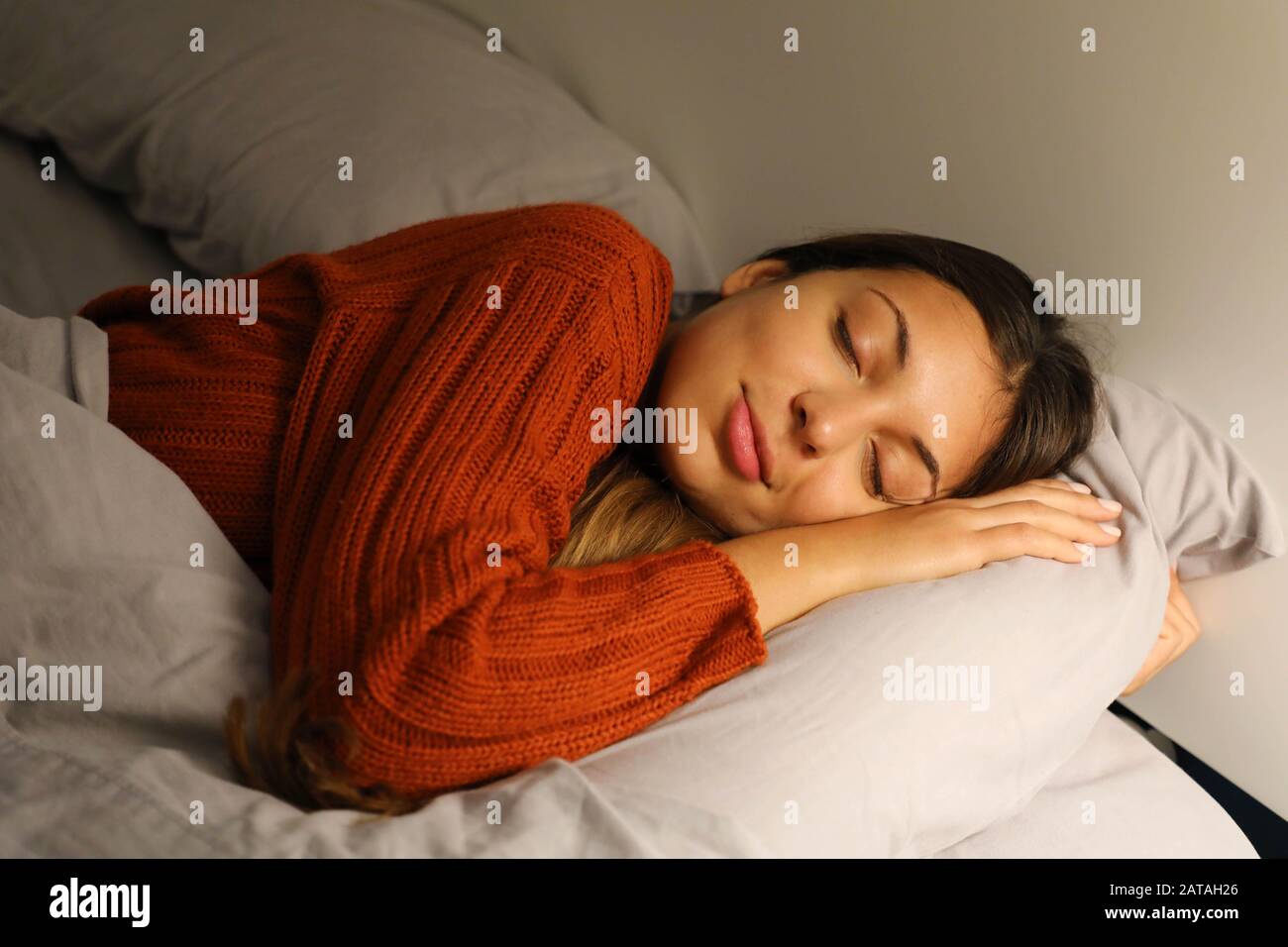 Pretty young woman sleeps hugging pillow on bed at night Stock Photo