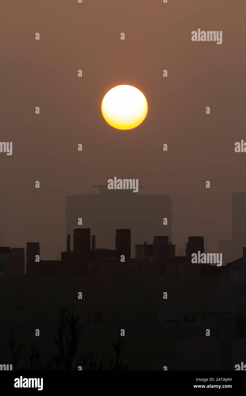 Sunset with a big round sun on a city with fog Stock Photo