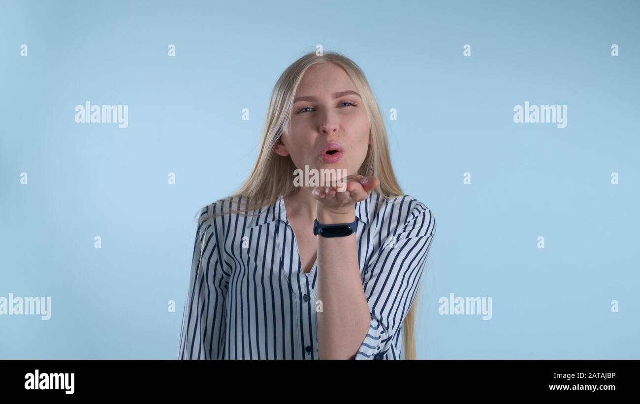 Young lady sending an air kiss and blinking with one eye on blue ...
