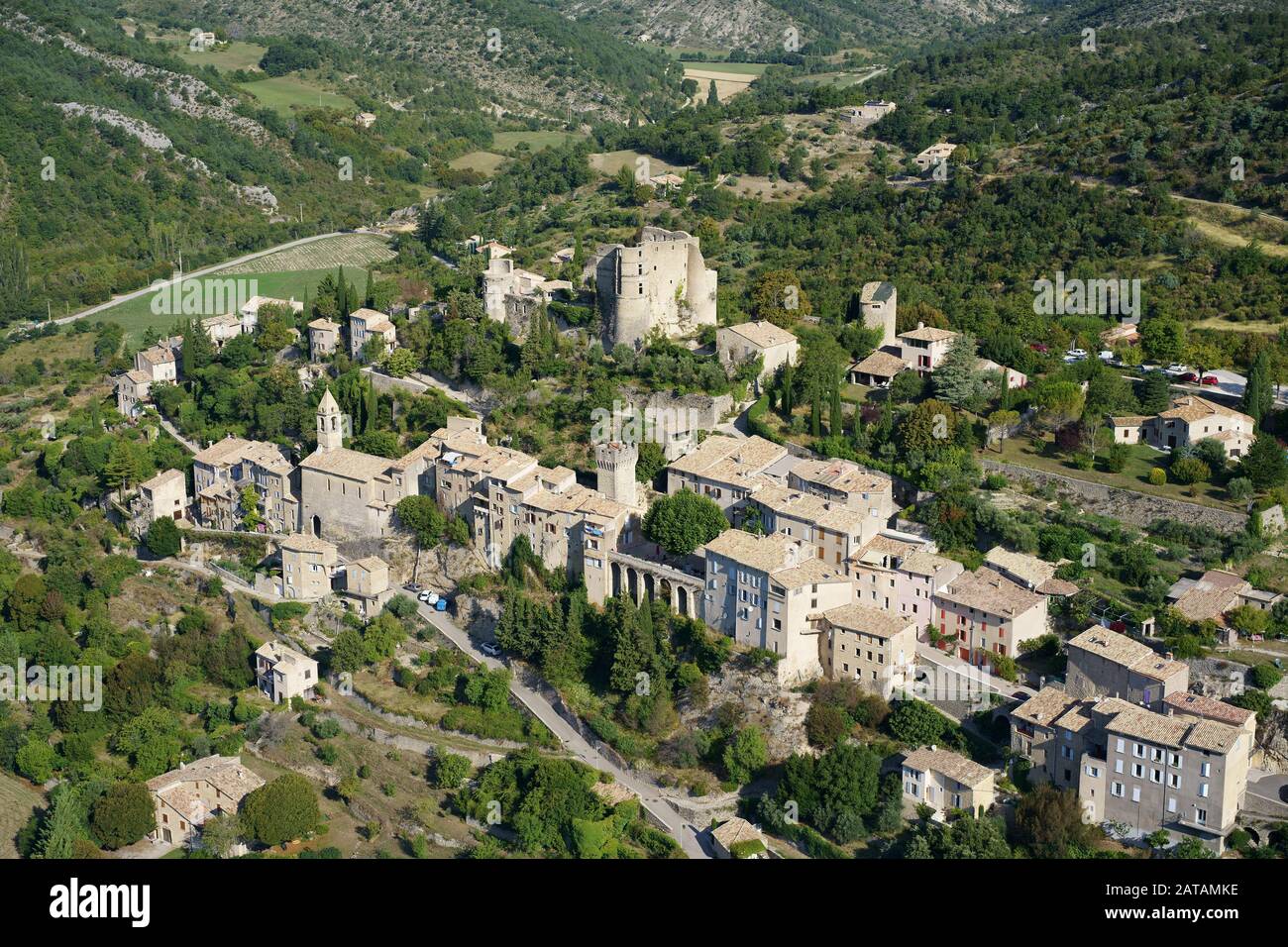 AERIAL VIEW. Provencal village built on a hill, crowned with a medieval castle in ruins. Montbrun-les-Bains, Drome, France. Stock Photo