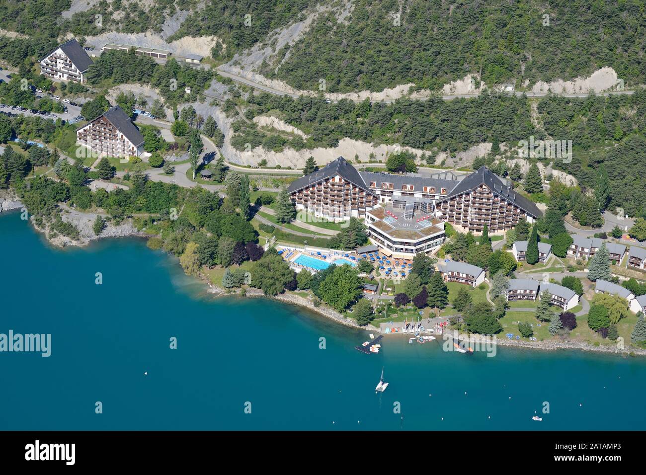 AERIAL VIEW. Holiday village on the lakeshore of Lake Serre-Ponçon. Les Hyvans, Hautes-Alpes, France. Stock Photo