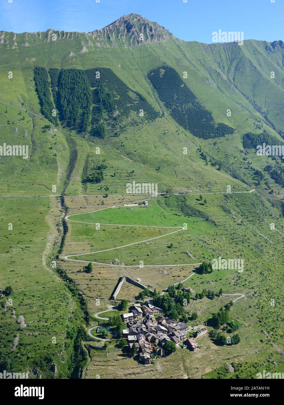 AERIAL VIEW. Small alpine village with a snow barrier for avalanche protection. Pequerel, Metropolitan City of Turin, Piedmont, Italy. Stock Photo