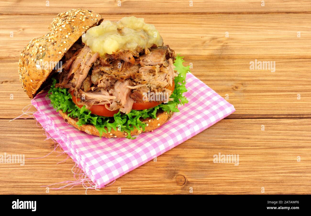 Hog roast meat sandwich with apple sauce and salad in a seed covered bread roll on a wooden background Stock Photo