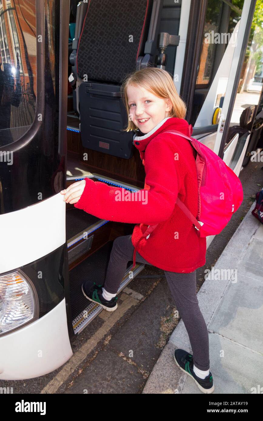 Year 5 Schoolgirl / girl / child / kid / student pupil aged nine years boarding a coach school bus at the start of a school trip. England UK. (107) Stock Photo