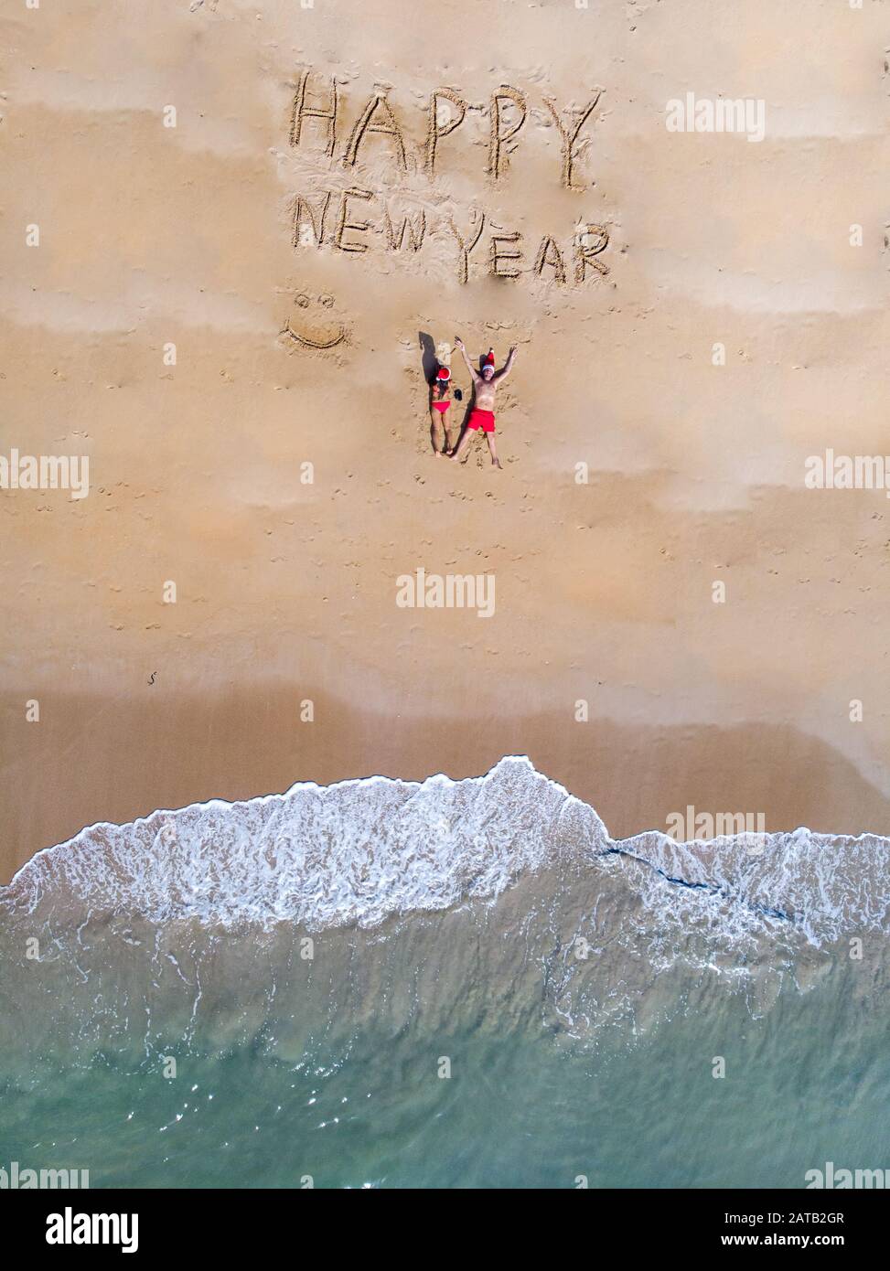 Happy new year sign on the beach with couple in the sand and chritmas ...