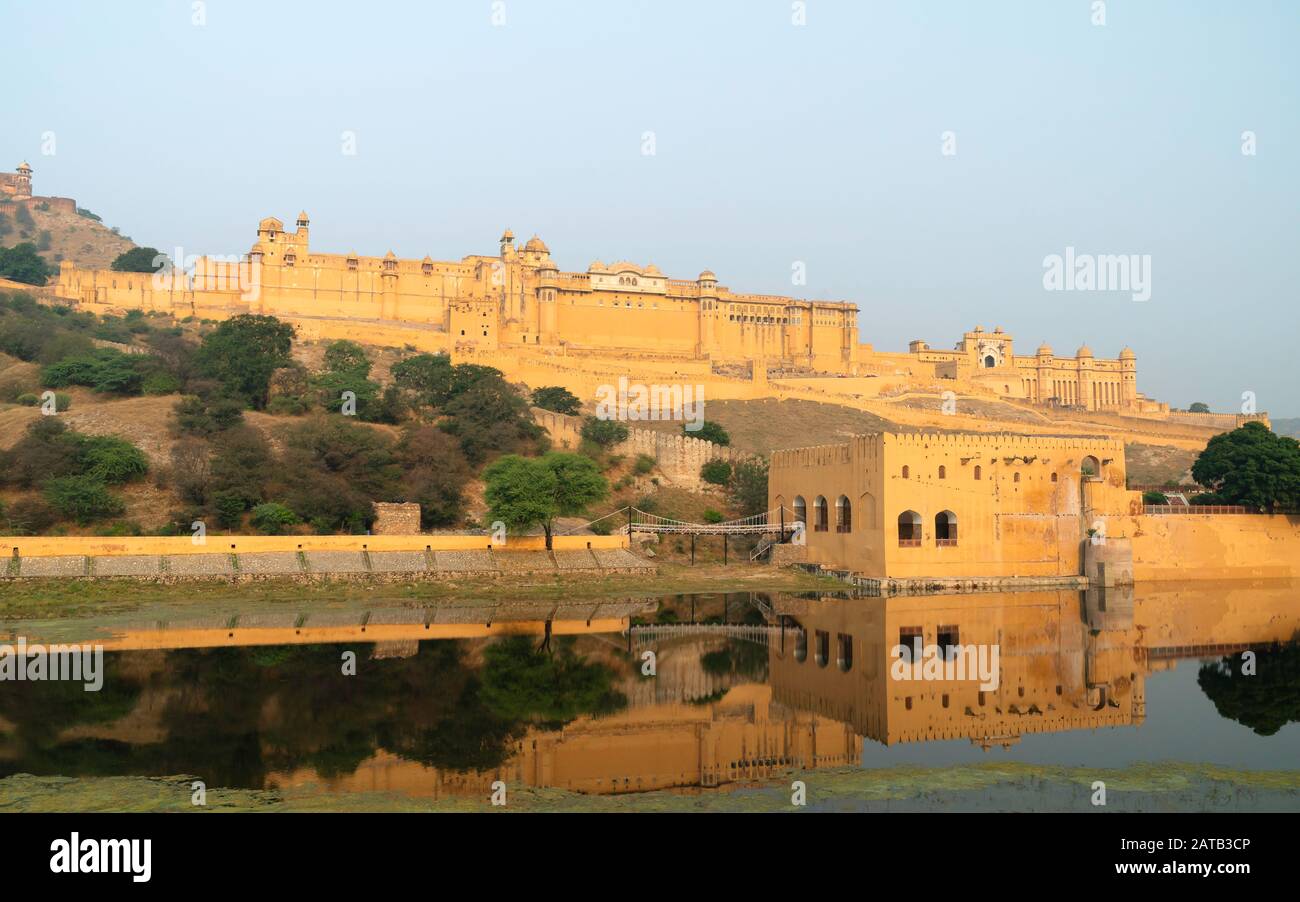 Amer Fort bathed in morning sunlight with view of trees and reflections in moat under blue sky in summer near Jaipur, Rajasthan, India. Stock Photo