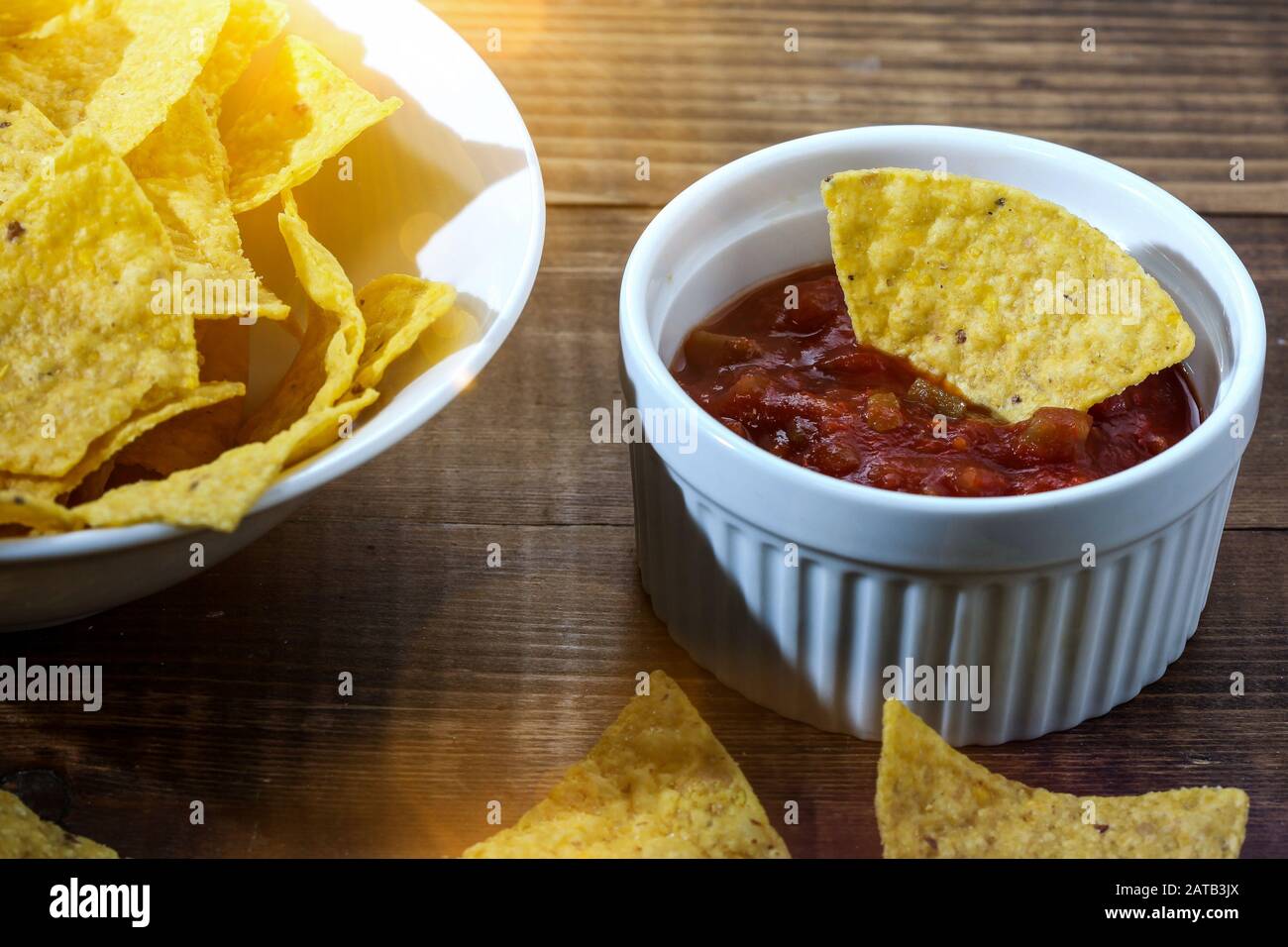 Tortilla chips inside bowl with salsa on wooden table with sun beam Stock Photo