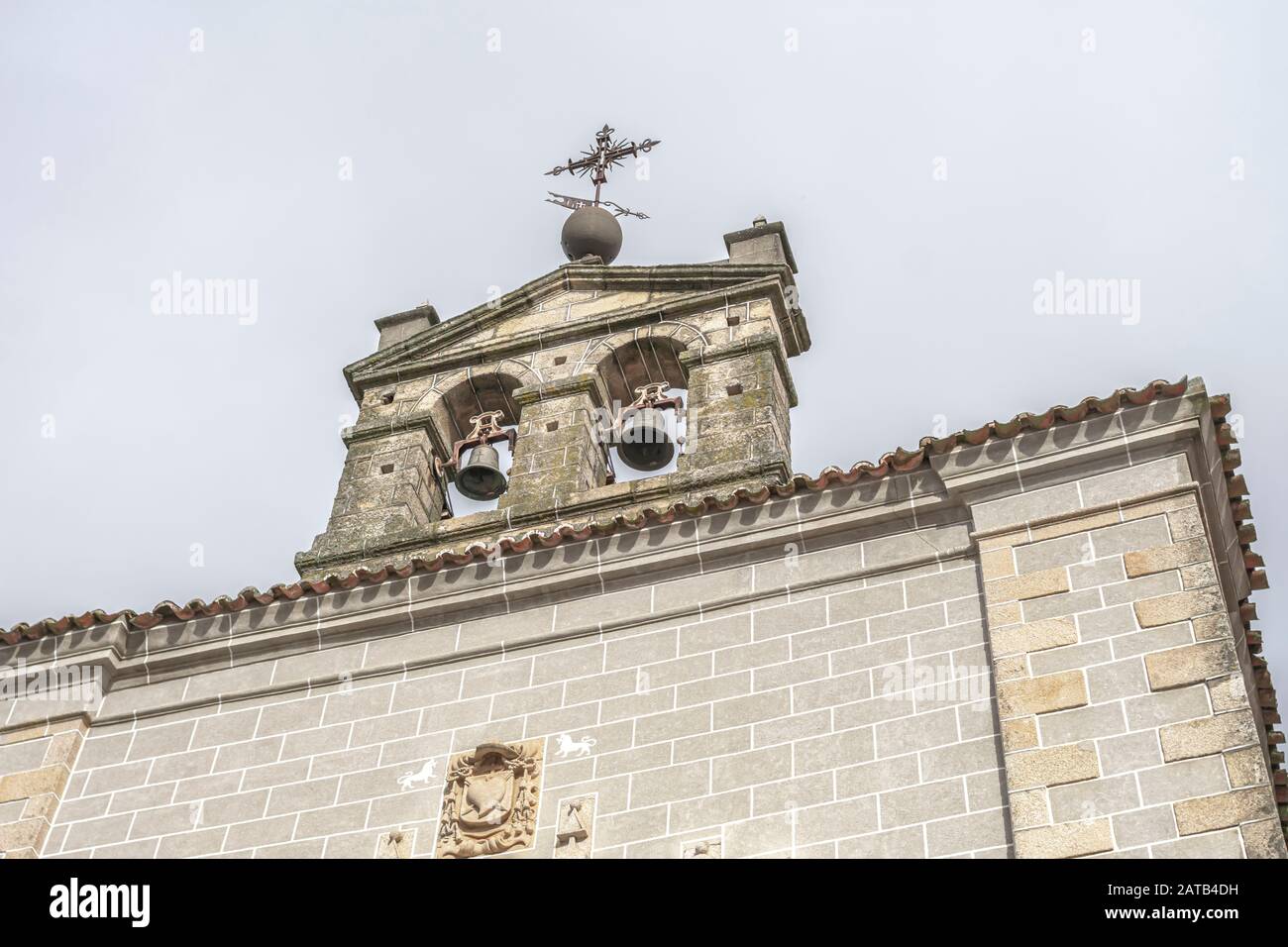 Bell tower of a church with a metal cross on top and details carved in stone on the facade, west of Spain, in Serradilla (Caceres) Stock Photo