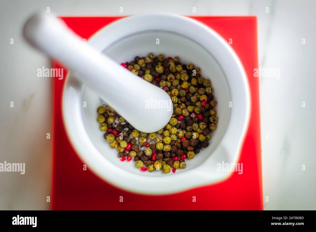 Colorful pepper in white mortar on red coaster, kitchen Stock Photo