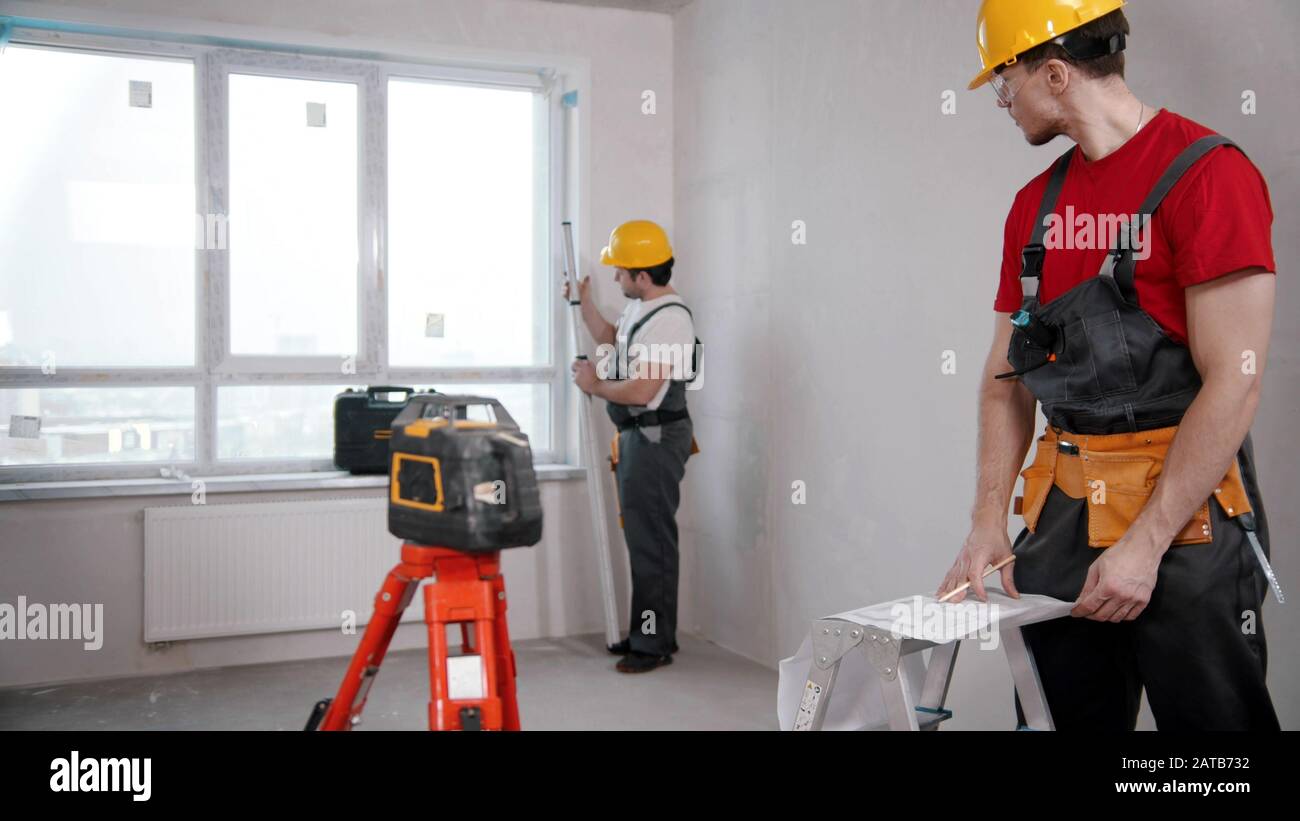 Two men workers measuring the distance from the windowsill to the ceiling and another writing notes about it Stock Photo