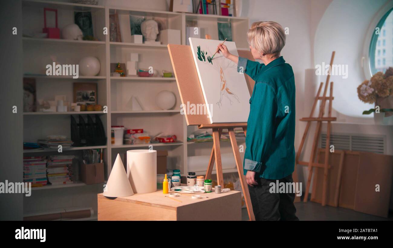 A young woman artist with short hair painting upper branches of tree in  green color in the art studio Stock Photo - Alamy